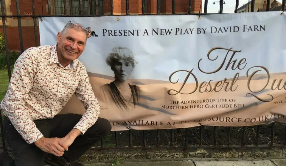 David Farn crouched in front of a poster advertising his play "The Desert Queen"